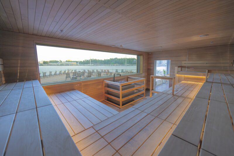 Allas Sea Pool — Finnish sauna interior with timber benches and a panoramic harbour-view window