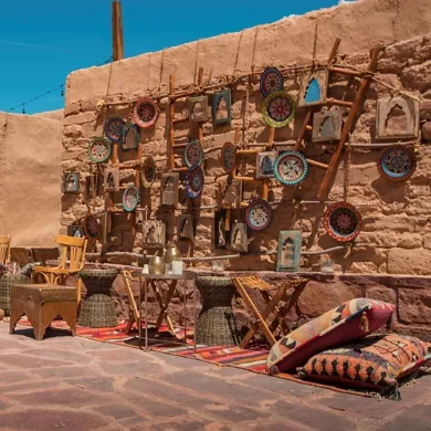 AlUla Old Town — mud-brick wall hung with hand-painted ceramic plates, woven cushions and a small wooden table on a rug