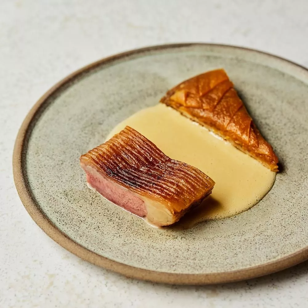 Arakataka — seared duck breast with crisp scored skin and pale sauce on a stoneware plate