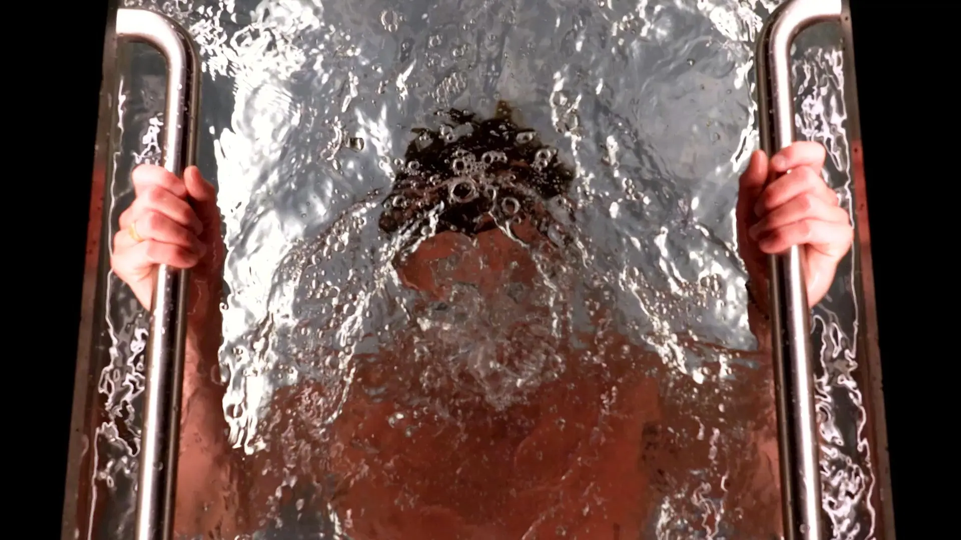 An overhead view of a Brass Monkey ice bath at ARC Canary Wharf, hands gripping the steel rails as cold water churns around the submerged head