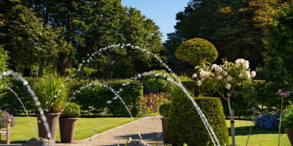 Ballynahinch Castle Hotel walled garden — sprinklers arcing over potted plantings, clipped topiary and a gravel path lined with summer roses