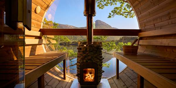 Barrel sauna at Ballynahinch Castle Hotel — open wood-burning stove framed by an arched window looking out across the Owenmore lake to the 12 Bens
