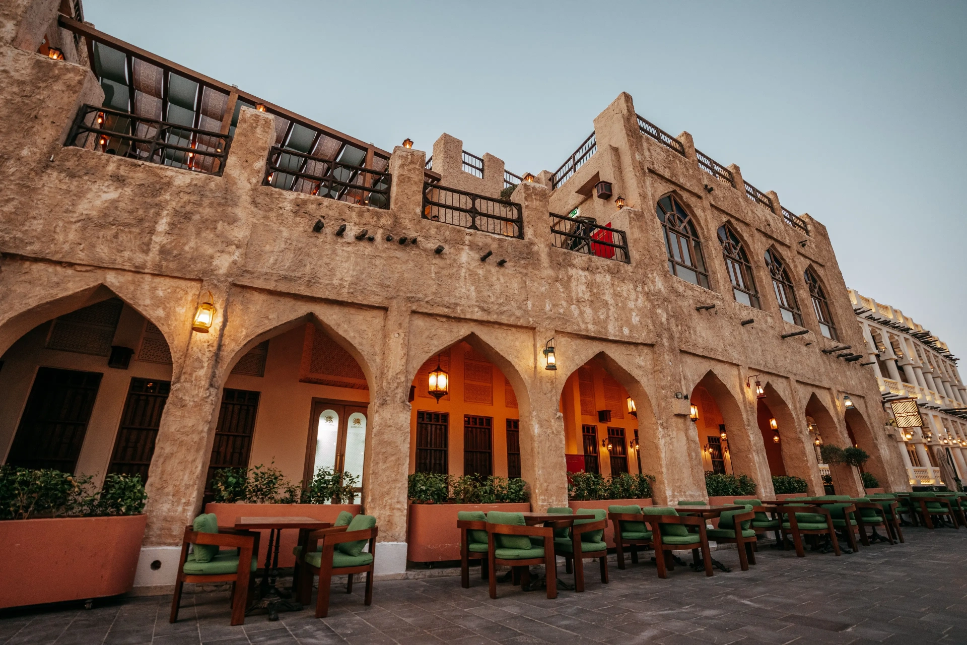 Berenjak Souq Waqif Doha — stone arcade facade with arched colonnade, lanterns and green-cushioned outdoor seating