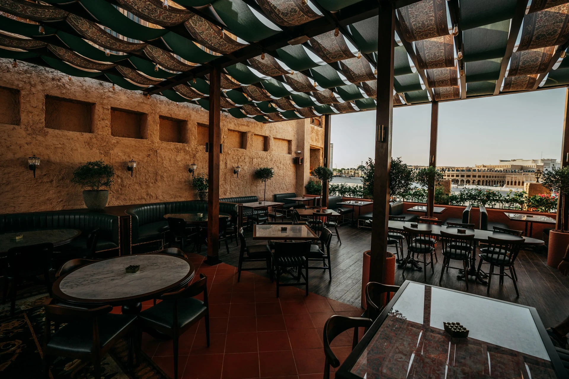 Berenjak Doha — covered outdoor terrace with patterned awning, banquette seating and views toward the Souq Waqif courtyard