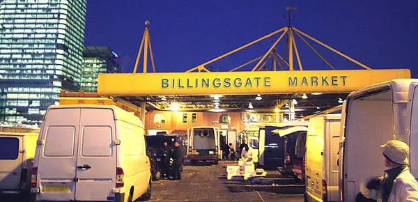 Billingsgate Market — vans and porters working under the lit entrance canopy before dawn