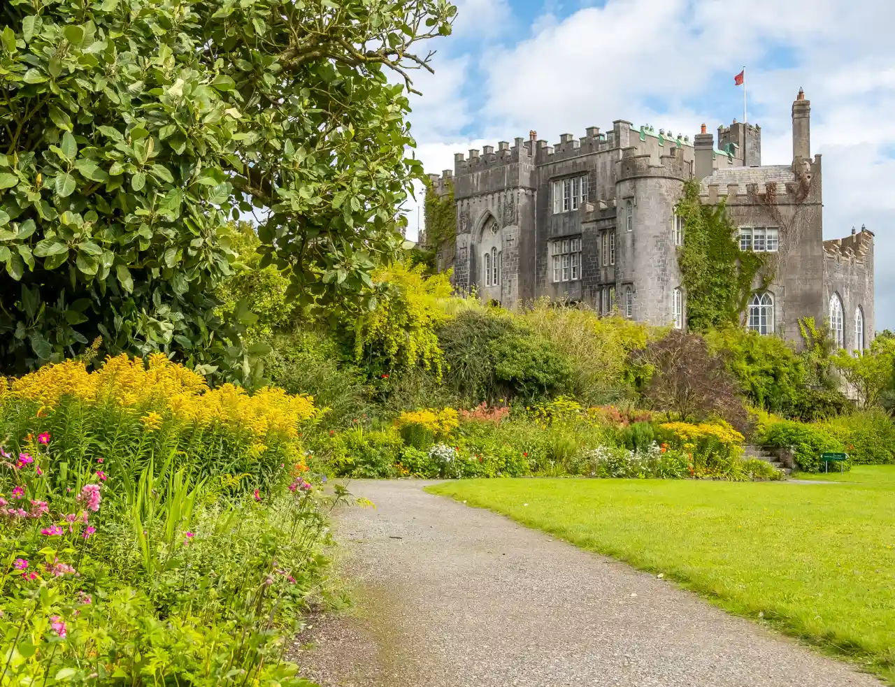 Birr Castle from the formal gardens — Gothic limestone facade rising above herbaceous borders of goldenrod, pink phlox and ornamental grasses
