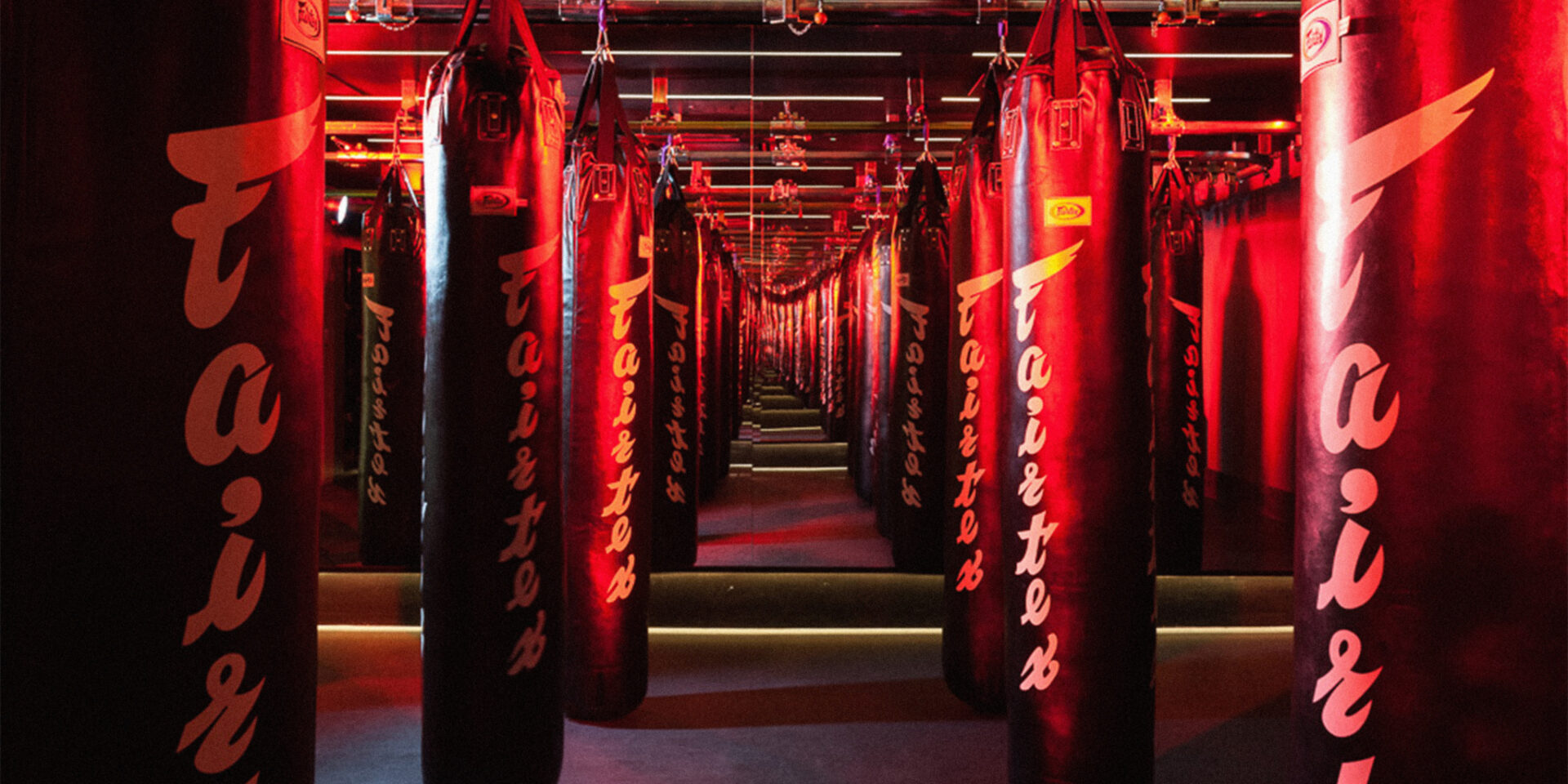 BXR Marylebone — an infinity corridor of Fairtex heavy bags lit in red, receding into mirrored reflection