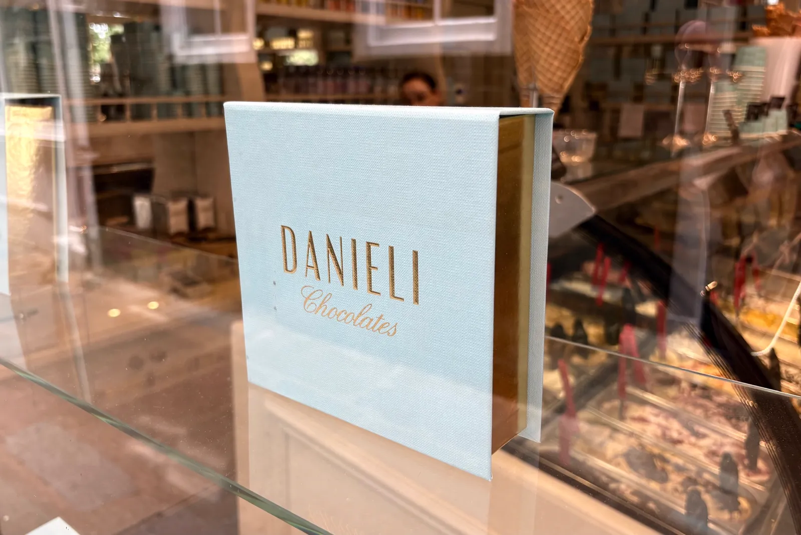 Danieli's bespoke pale-blue chocolate gift boxes tied with pink ribbons on a glass counter above trays of foil-wrapped and cocoa-dusted chocolates