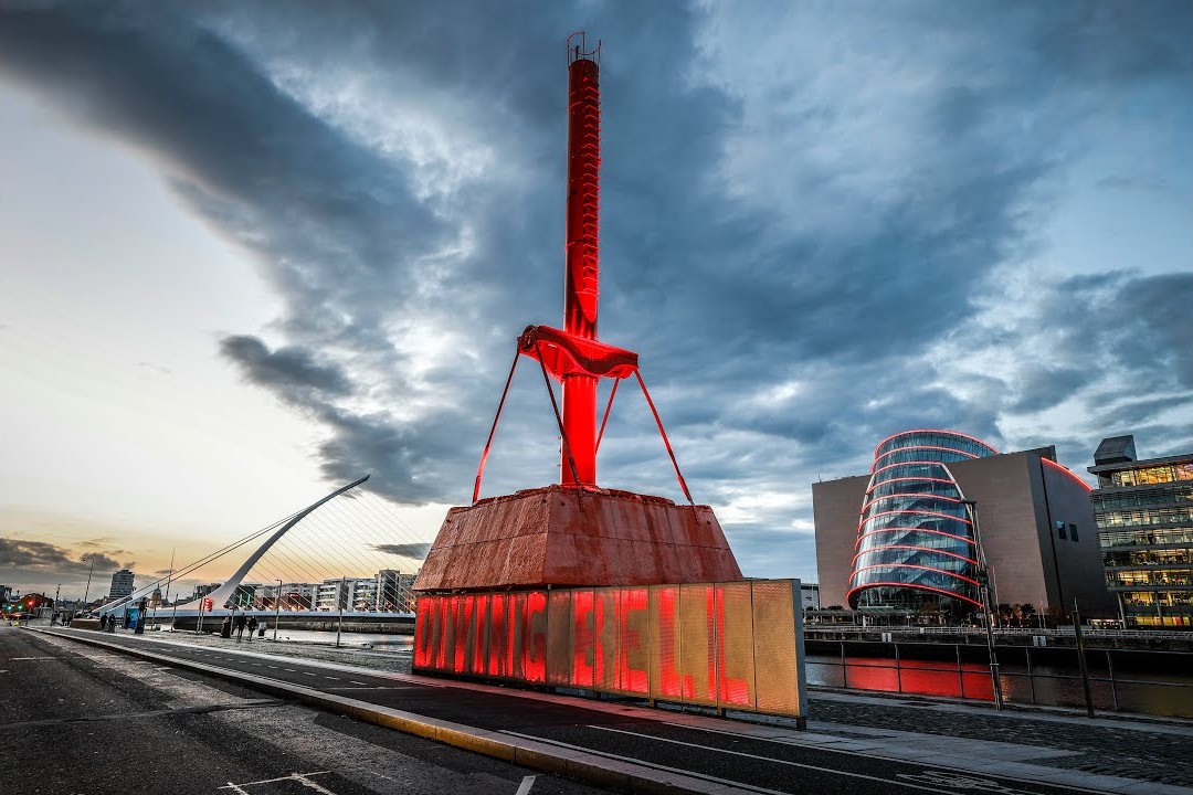 The restored Diving Bell on Sir John Rogerson's Quay in the Dublin Docklands, lit red at dusk with the Samuel Beckett Bridge and the Convention Centre Dublin behind