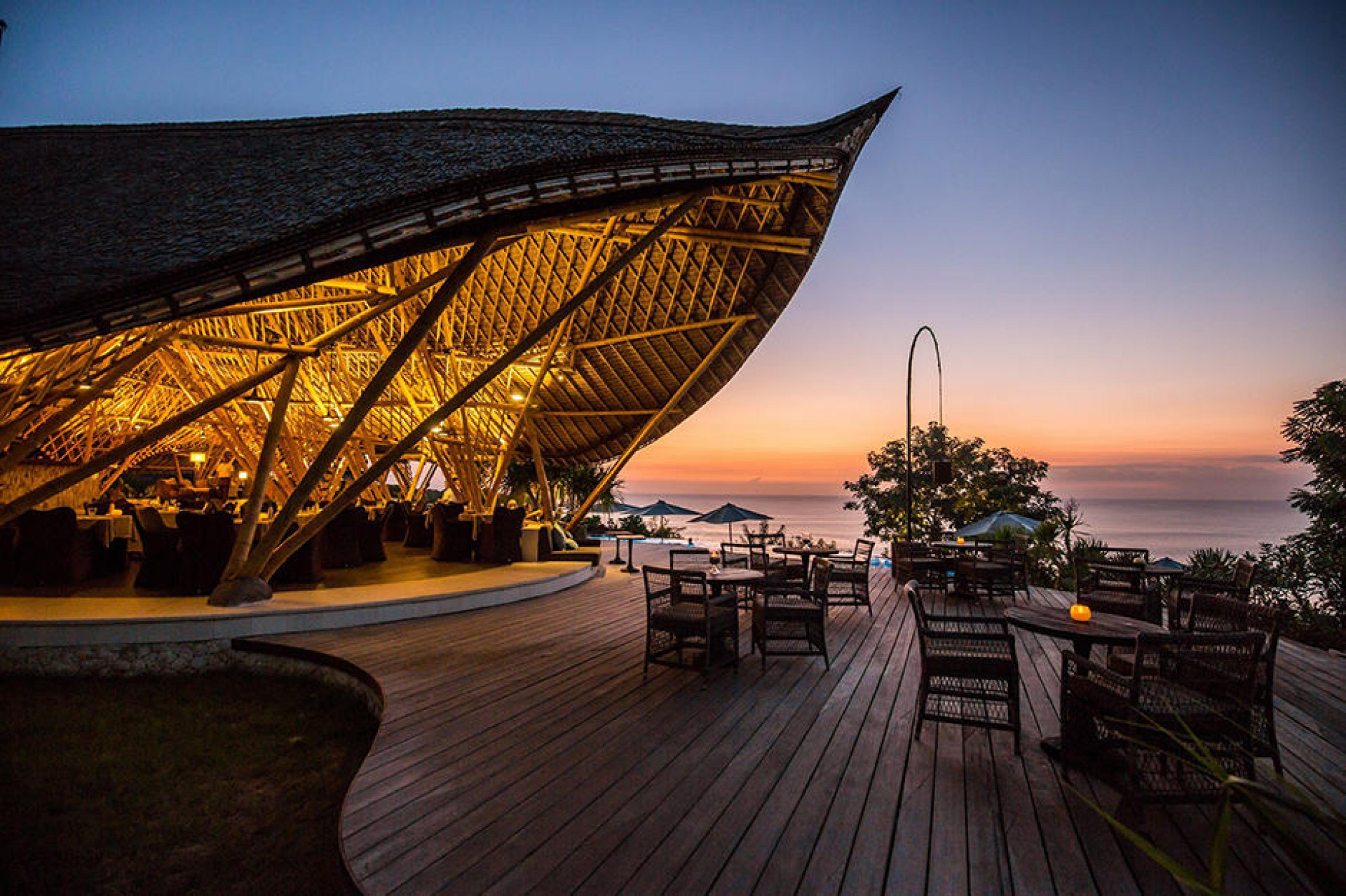 Dugong restaurant terrace at dusk — lit bamboo structure, timber decking and tables facing the Indian Ocean at sunset