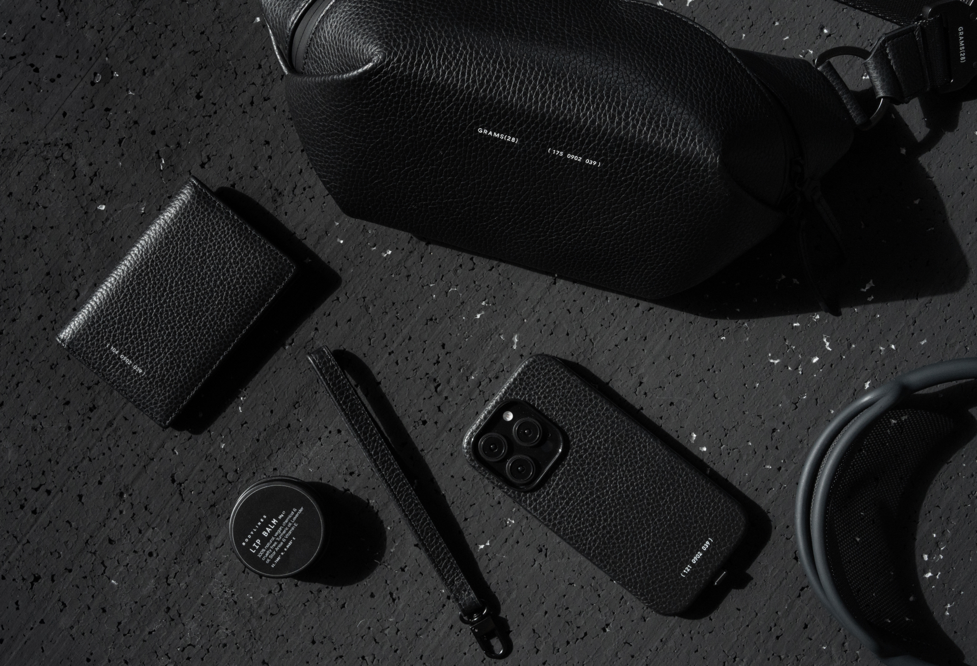 Grams28 accessories flatlay — sling bag, card holder, phone case, pen loop and headphones on dark terrazzo