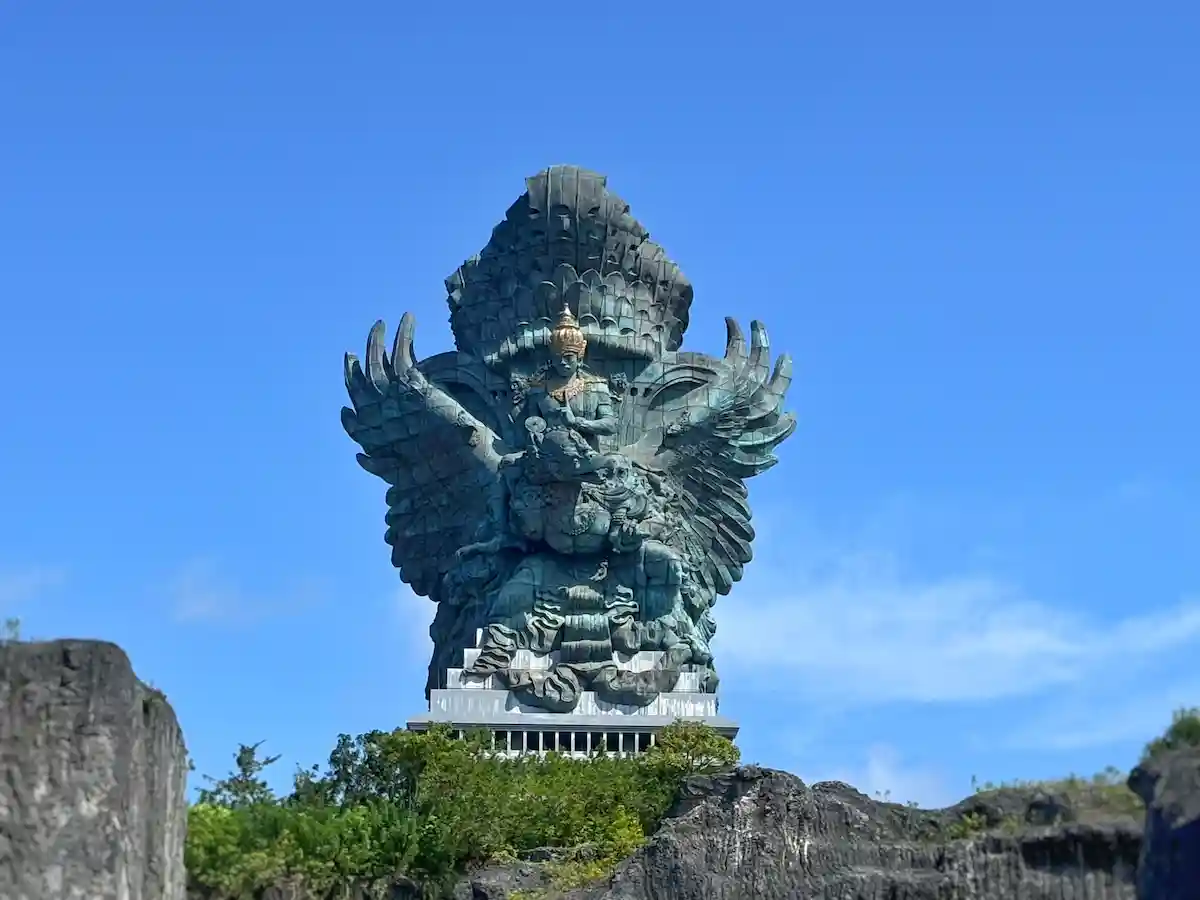 Garuda Wisnu Kencana statue front view — copper and brass Vishnu riding Garuda against blue sky