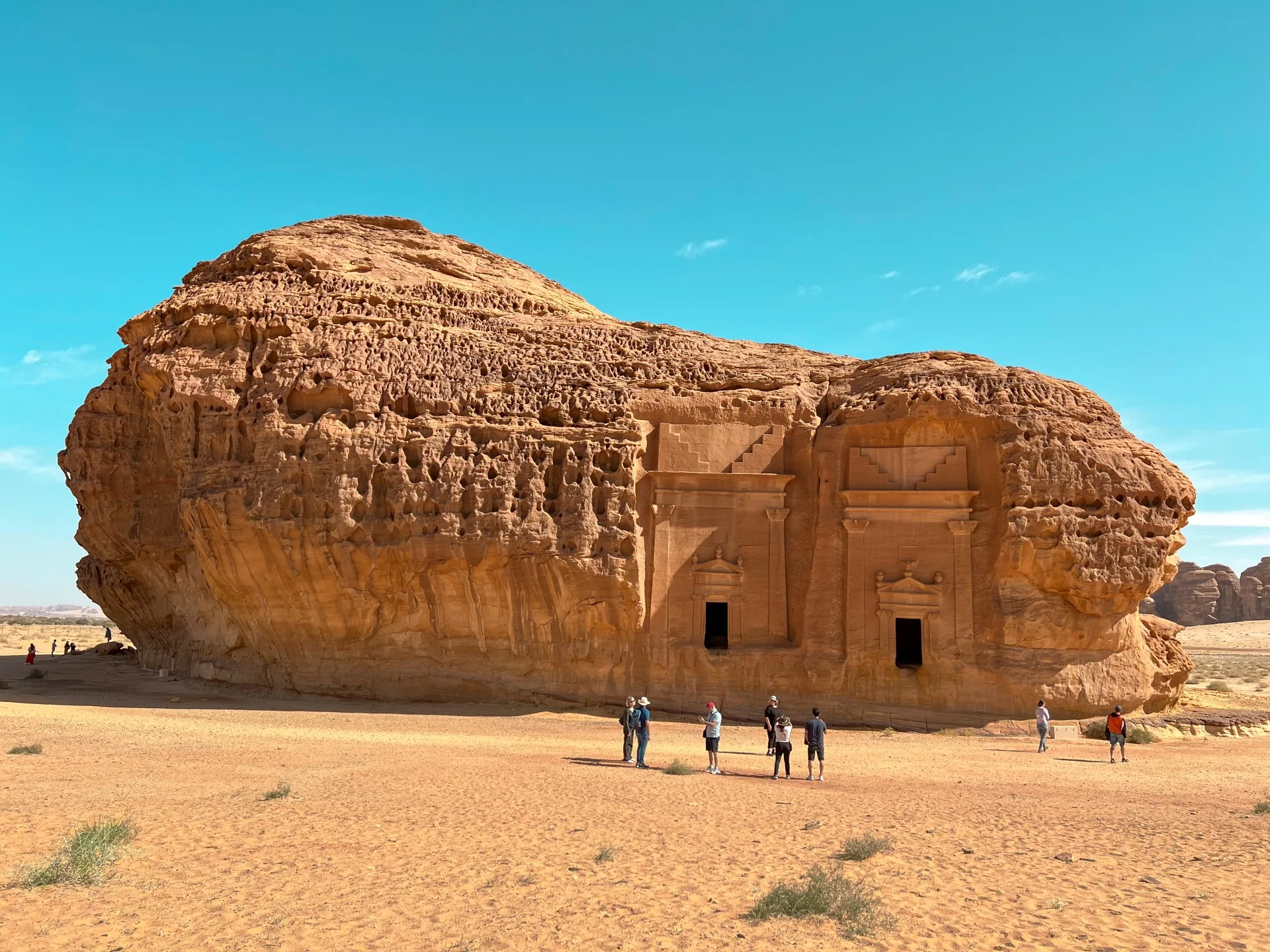 Hegra — Jabal Al-Ahmar, a free-standing sandstone massif with two carved Nabataean tomb facades and visitors for scale
