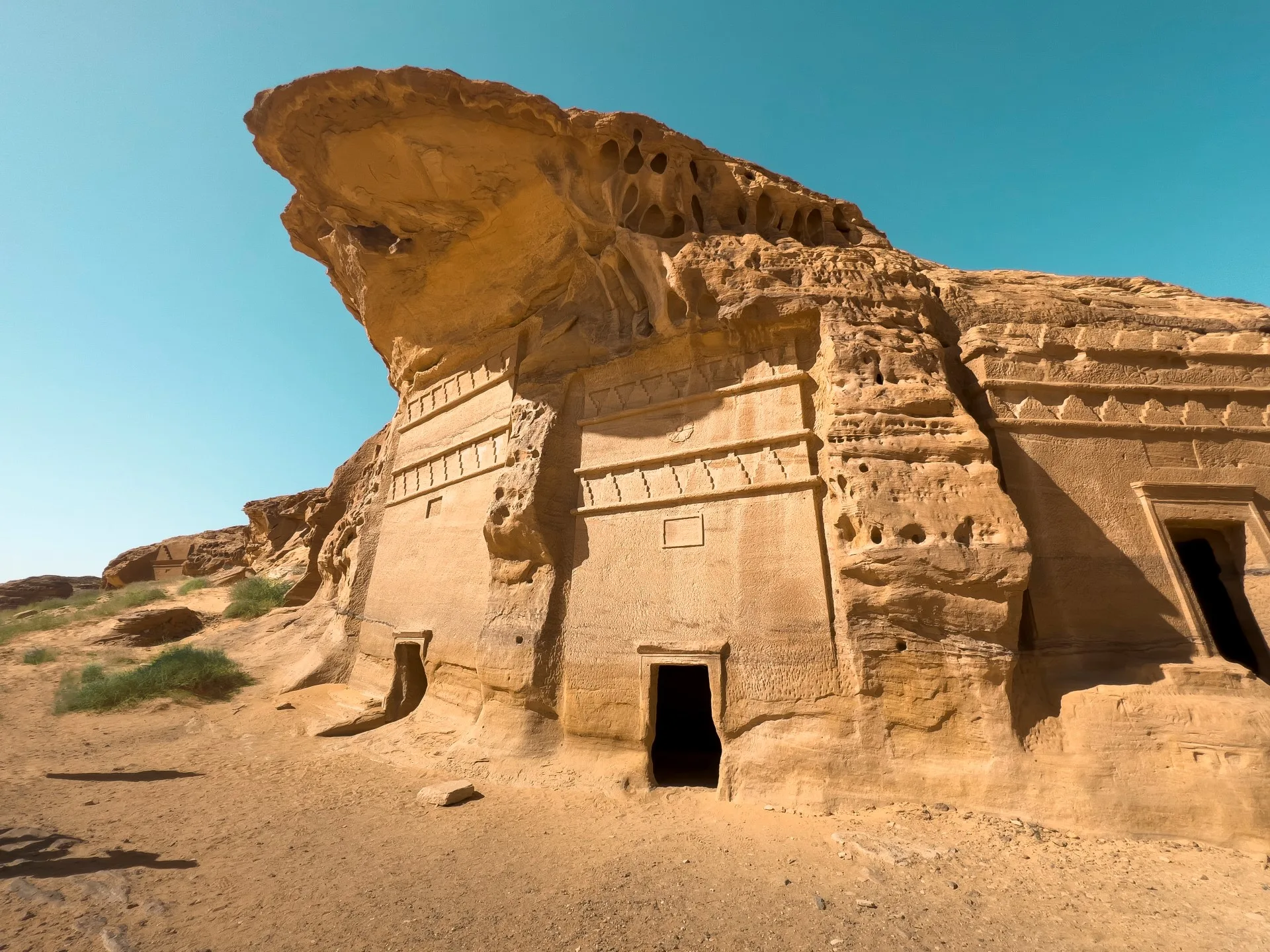 Hegra — Jabal Al-Banat tomb cluster, decorated Nabataean facades carved under an overhanging sandstone canopy