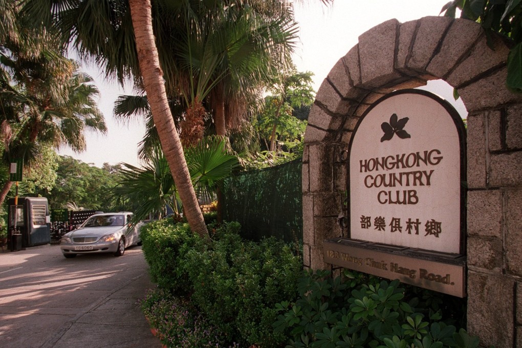 The stone entrance sign of Hong Kong Country Club at 188 Wong Chuk Hang Road, with a car passing the gatehouse beneath palm trees