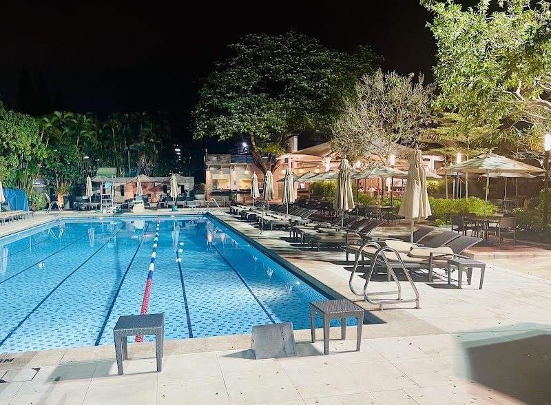 The outdoor swimming pool at Hong Kong Country Club at night, lit loungers and dining terraces beside it