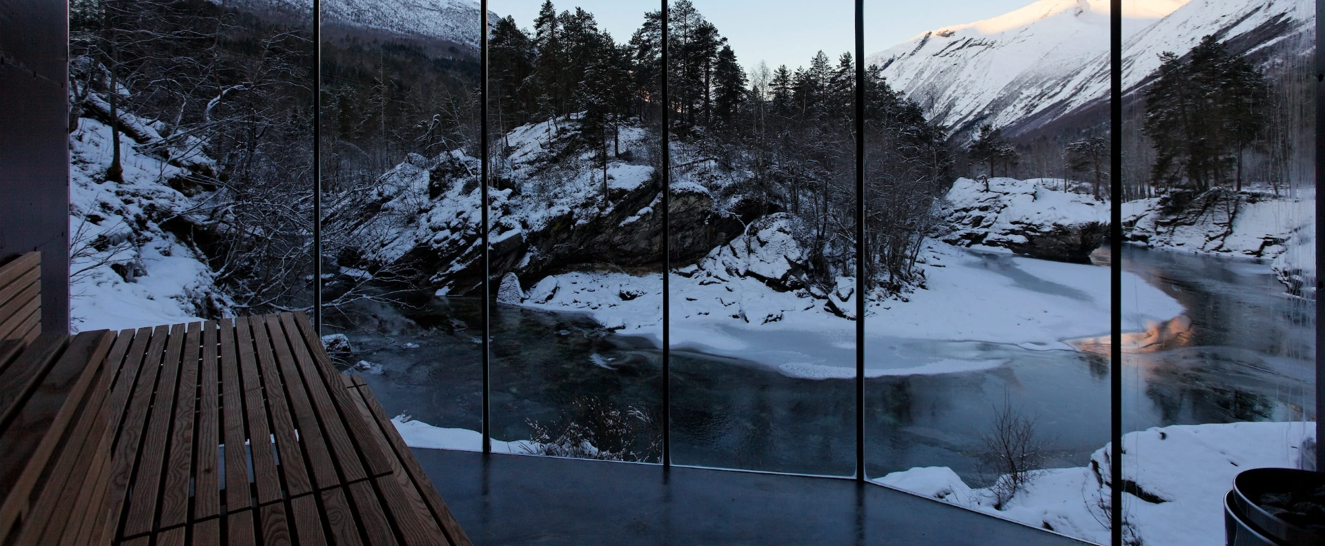 Juvet Bath House — glass wall framing the frozen Valldal river in winter