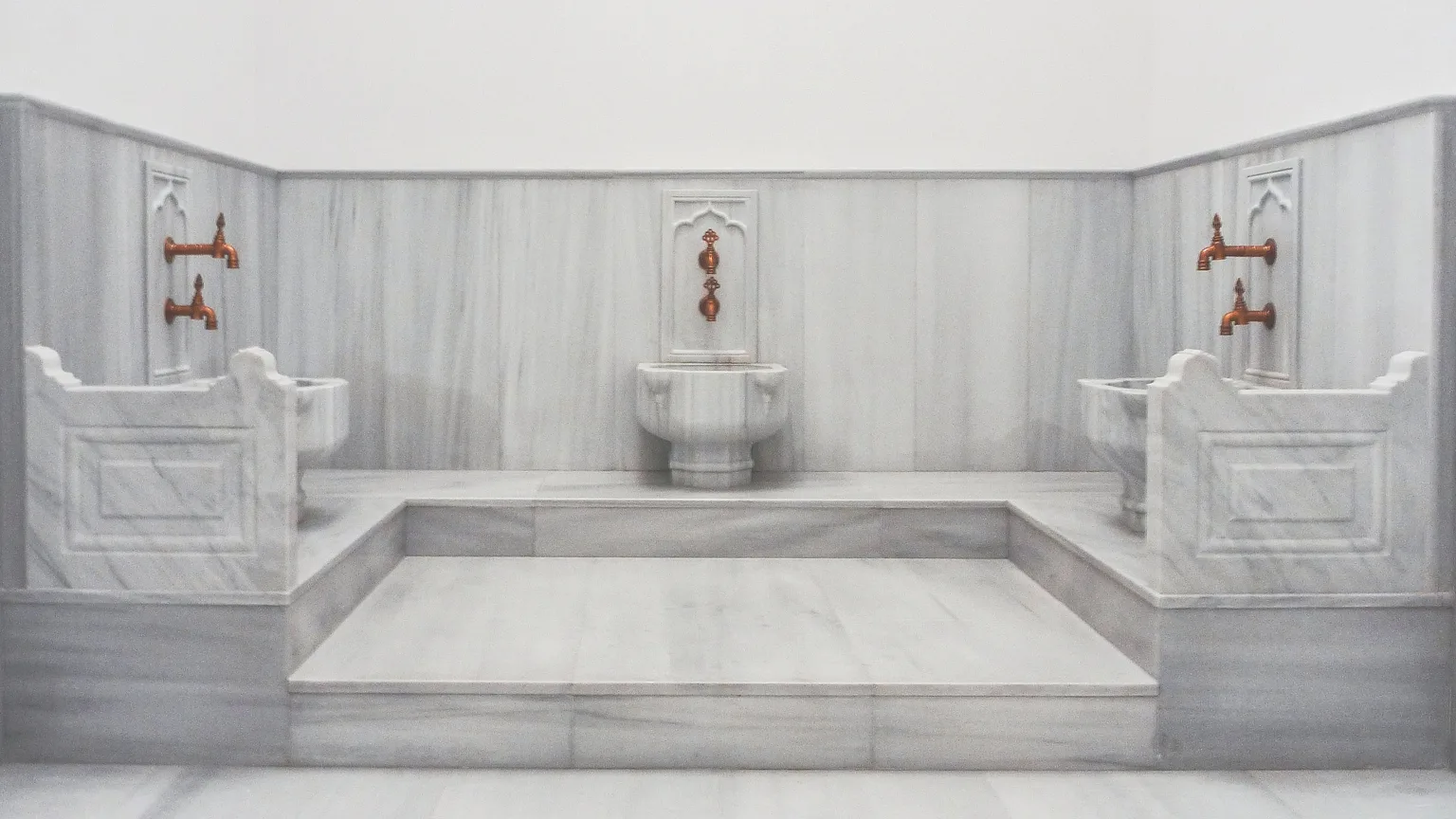 Kılıç Ali Paşa Hamamı — marble washing basins with copper taps against the pale marble walls