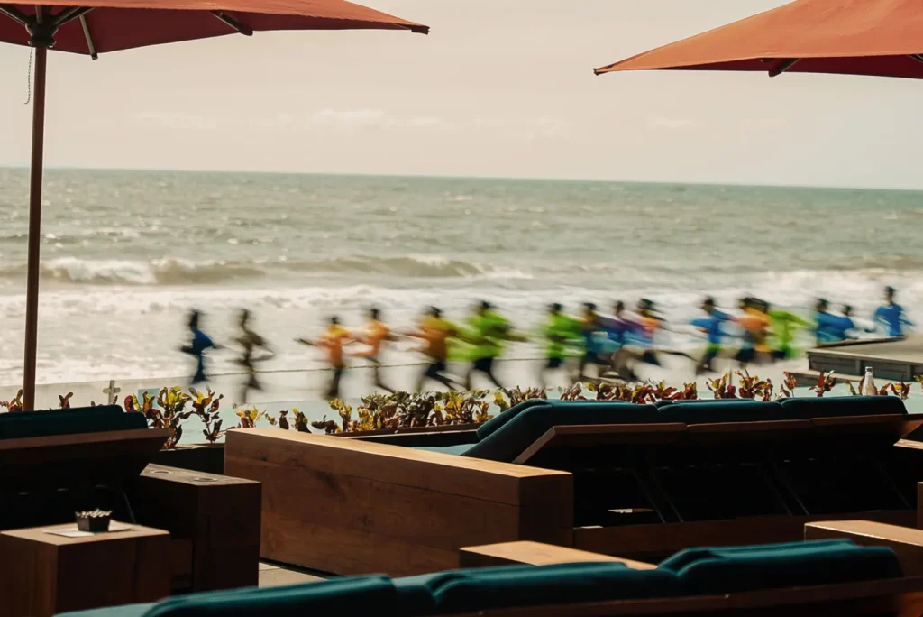 Runners passing the daybeds at Ku De Ta during a beachfront event