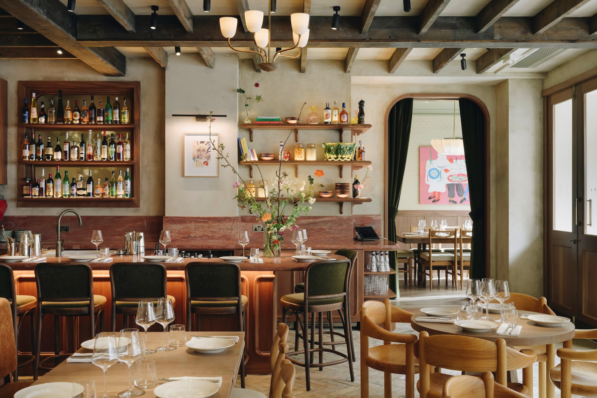Lita's bar and back dining room — an arched green-curtained doorway framing a second room hung with a large pastel painting, wooden bentwood bar stools with olive-green velvet seats, and open shelves of ceramics and glassware