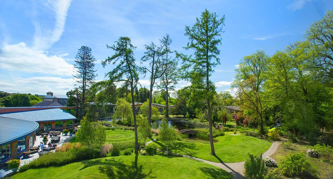 Summer view of the manicured gardens and woodland setting at Monart Destination Spa, with the property's contemporary spa wing on the left