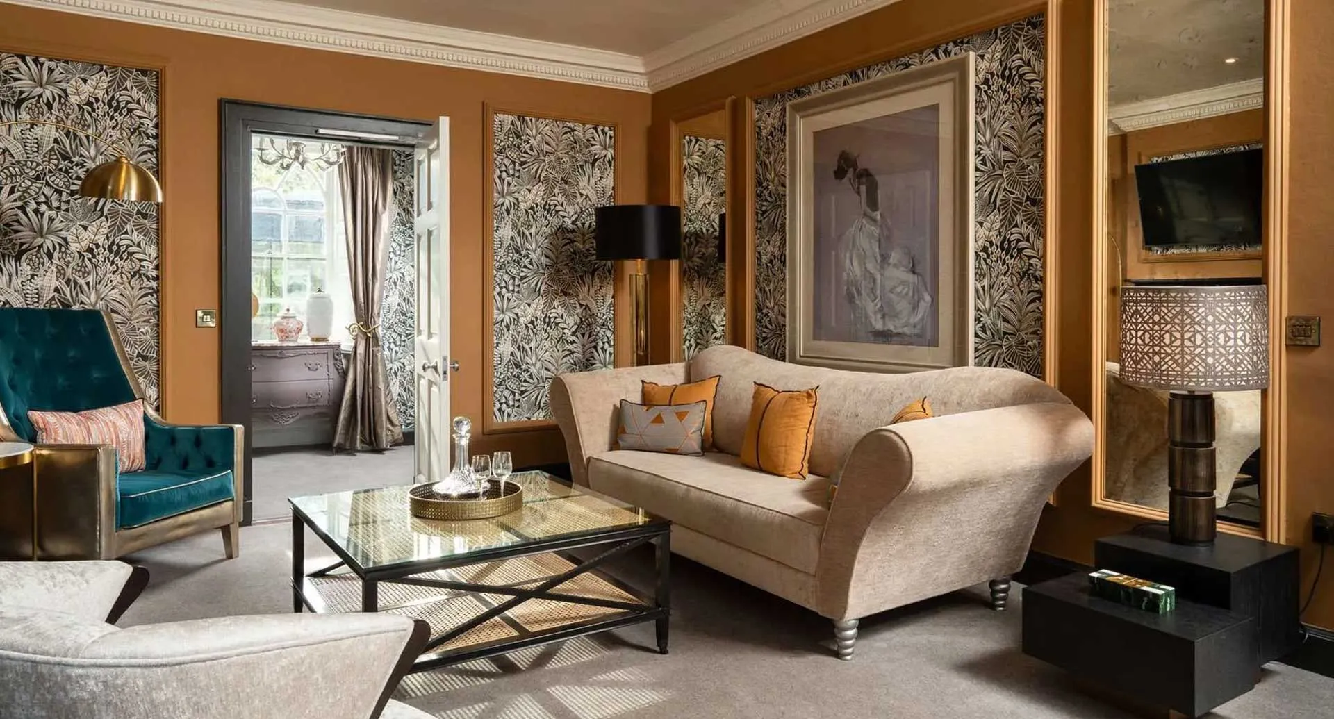 Interior of a luxury suite at Monart Destination Spa — warm terracotta walls, botanical wallpaper, a cream sofa and tufted teal armchair in the Georgian manor