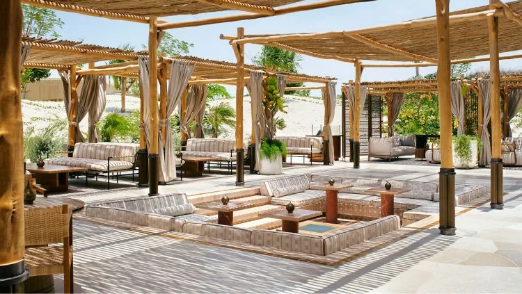 Nujuma — jamaa outdoor majlis terrace with bamboo pergola, sunken seating and striped cushions overlooking the dunes