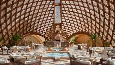 Nujuma — interior of the SITA central pavilion with woven timber lattice dome, hanging lanterns and a central fountain