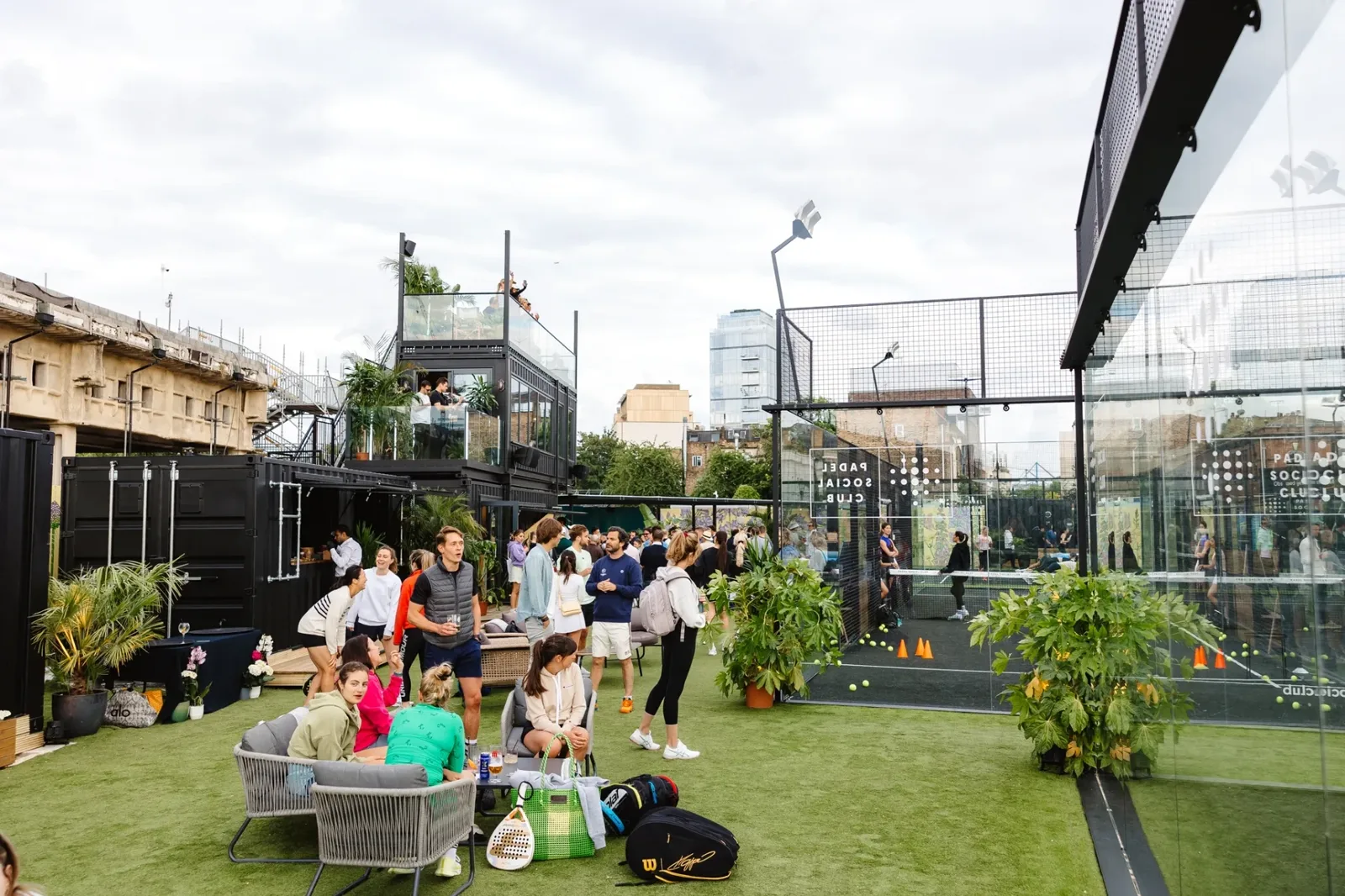 Padel Social Club Earl's Court — the two-storey container clubhouse, lawn seating and glass court alongside
