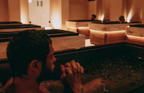 Rebase Recovery — a member submerged to the shoulders in a marble ice bath, hands clasped, warm ambient light behind