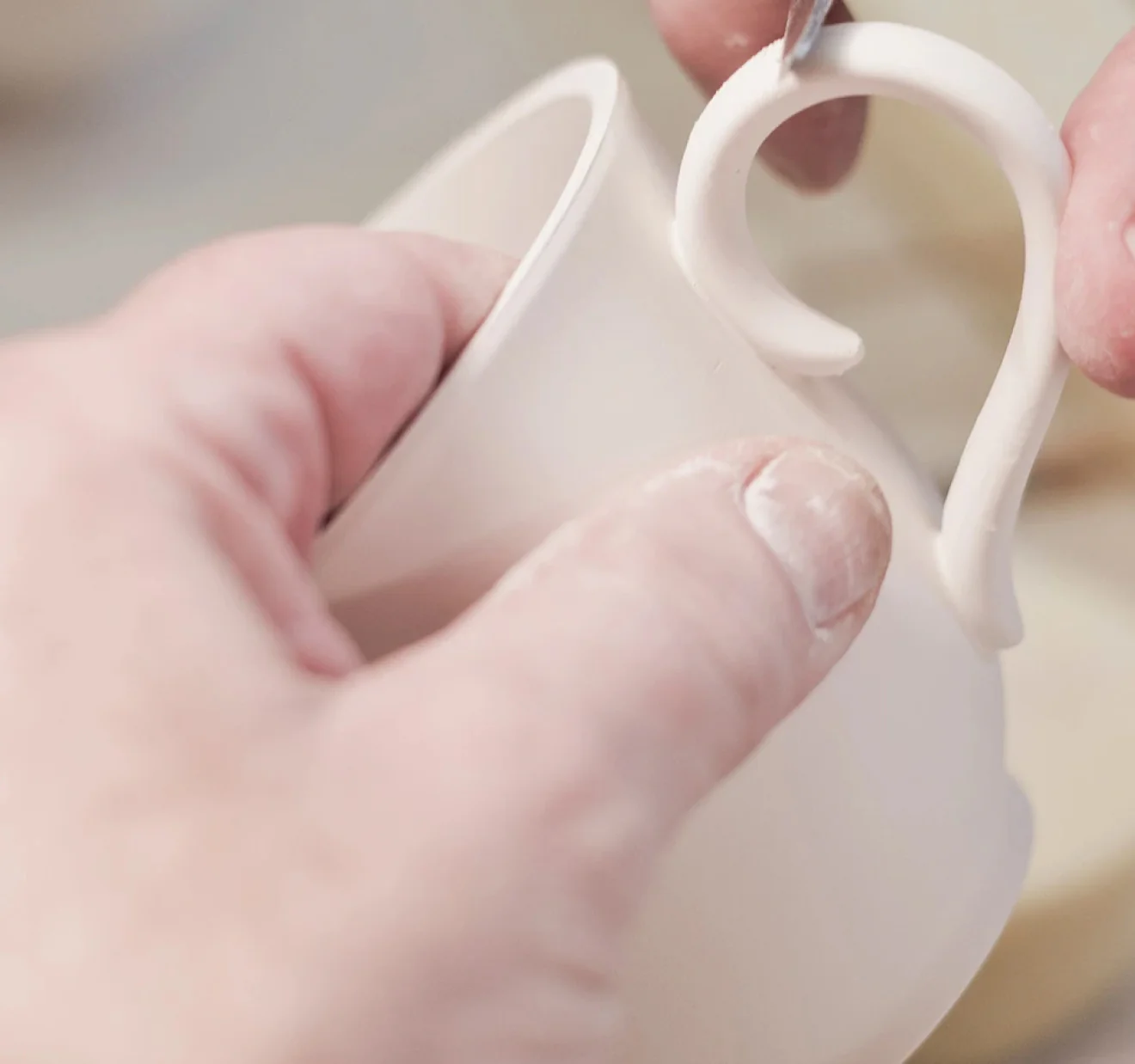 Hands carefully shaping the handle of a Richard Brendon bone china cup during production