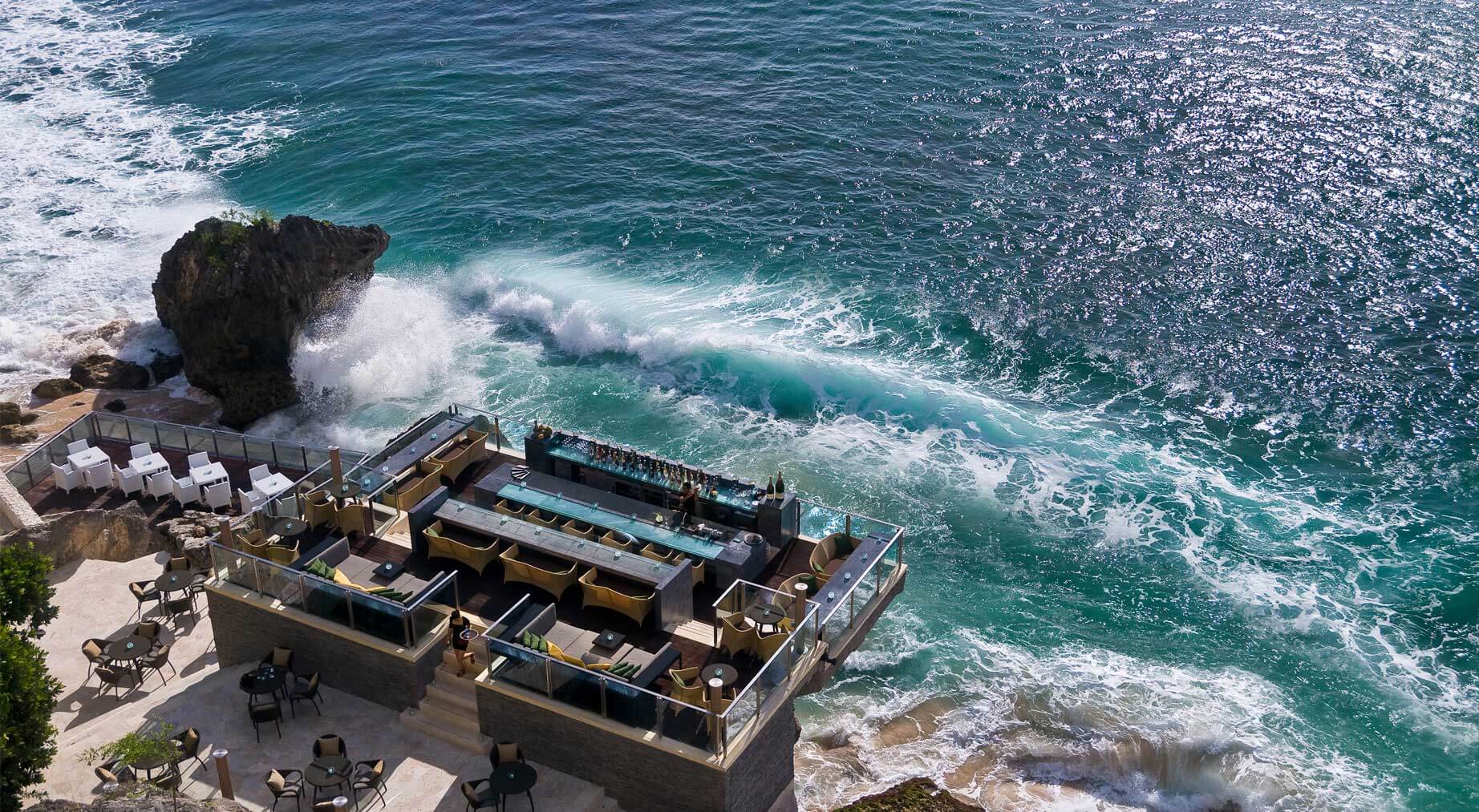 Rock Bar at AYANA Jimbaran — aerial daytime view of the bar carved into the limestone cliffs of Jimbaran Bay above the Indian Ocean