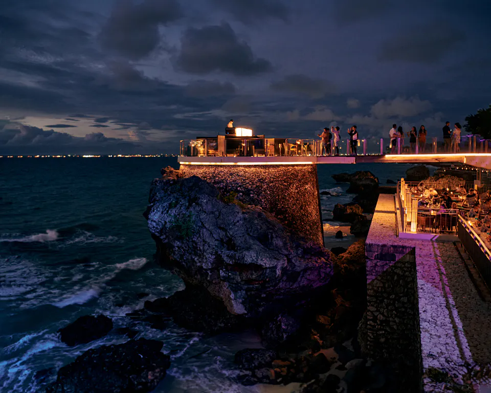 Rock Bar at AYANA after dark — the lit cliff platform with guests at the edge above the Indian Ocean at Jimbaran
