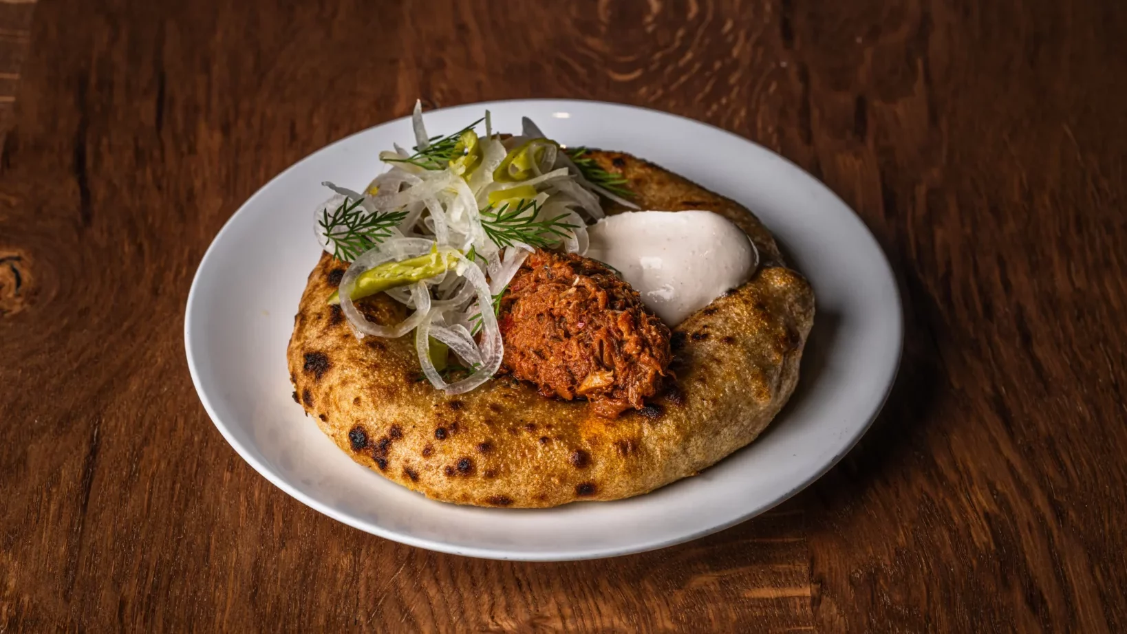 A smoked mackerel flatbread at Roe — golden charred flatbread topped with a quenelle of pink-orange mackerel, shaved white onion, dill, sliced green chilli and a quenelle of cool white crème fraîche, on a dark wooden table