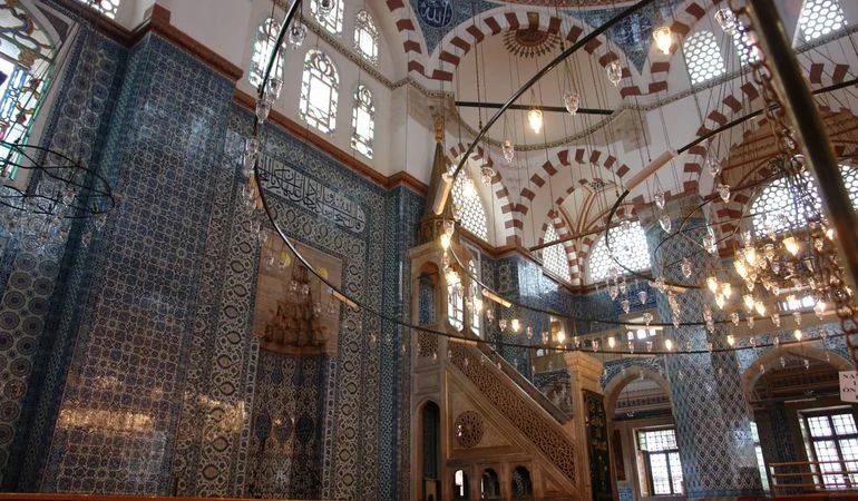 Rüstem Pasha Mosque interior — Iznik tiled walls, the carved minbar and hanging lamps beneath the dome