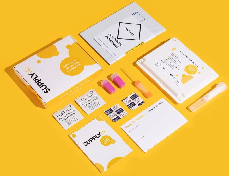 Supply Life food intolerance test kit contents — box, sample collection pack, lancets, alcohol wipes and biological substance envelope, flat-lay on yellow