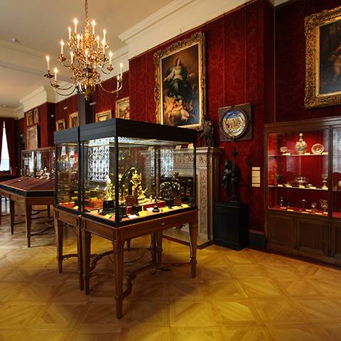 The Wallace Collection's Sixteenth Century Gallery — dark red walls, a chandelier, and glass vitrines of bronzes and decorative objects