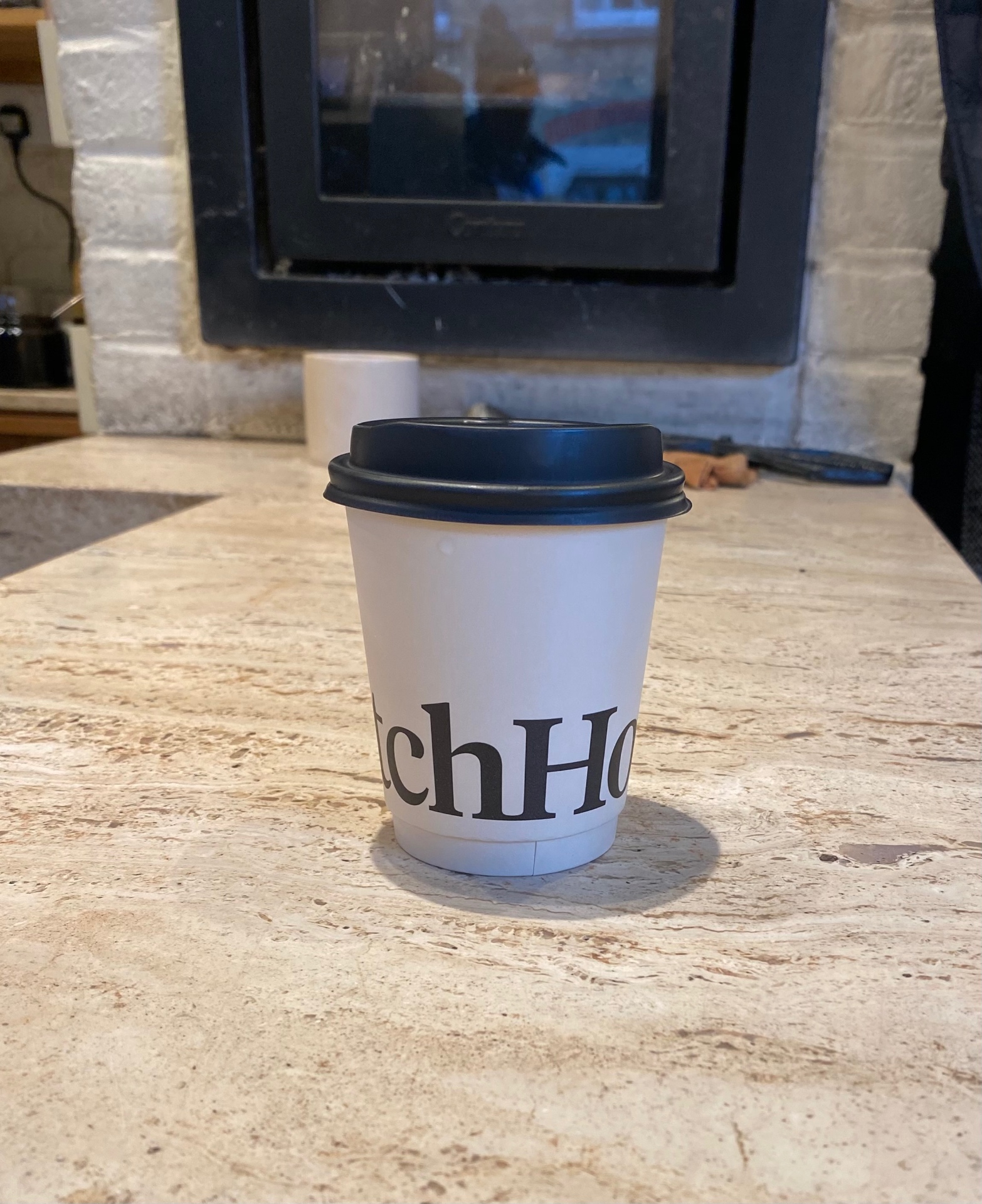 WatchHouse branded coffee cup on marble counter with fireplace in background