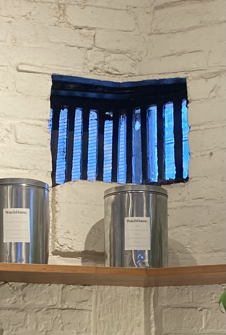 Original barred window with WatchHouse coffee tins on wooden shelf against white brick wall