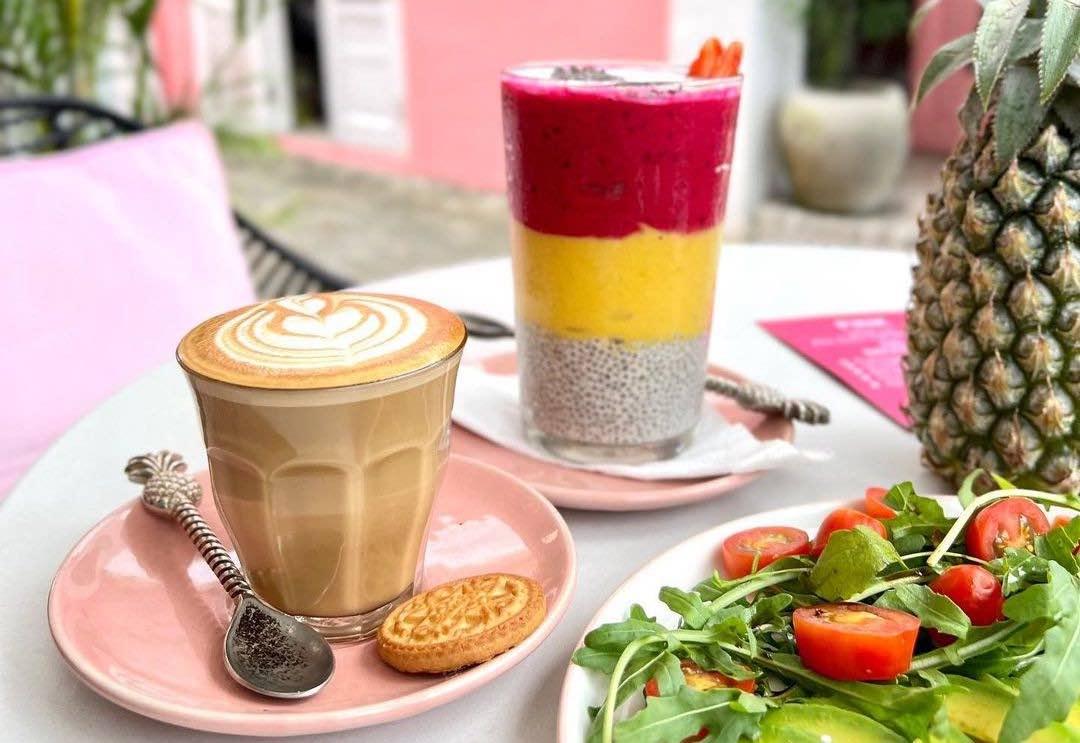 Doppio Pink Café, Canggu — latte, layered smoothie and salad on a pink-tiled table
