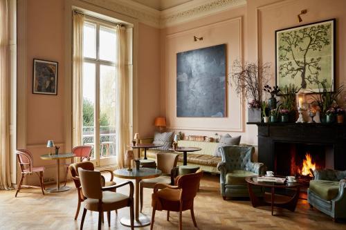 The drawing room at Bingham Riverhouse — high pale-pink walls, tall windows, mismatched armchairs and small café tables, a lit fireplace and a large abstract painting above