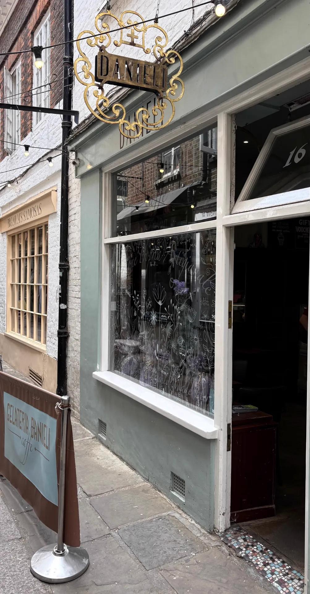 Gelateria Danieli on Brewers Lane, Richmond — a narrow cobbled alley strung with festoon lights, the gelateria's ornate gold-scrolled sign hanging above a pale shopfront with small round pavement tables and leather-topped stools