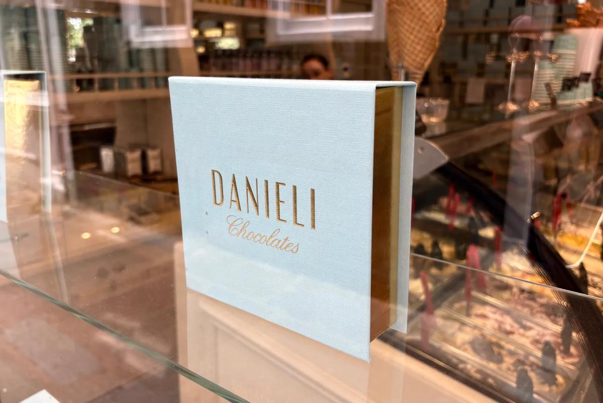 Danieli's bespoke pale-blue chocolate gift boxes tied with pink ribbons on a glass counter above trays of foil-wrapped and cocoa-dusted chocolates