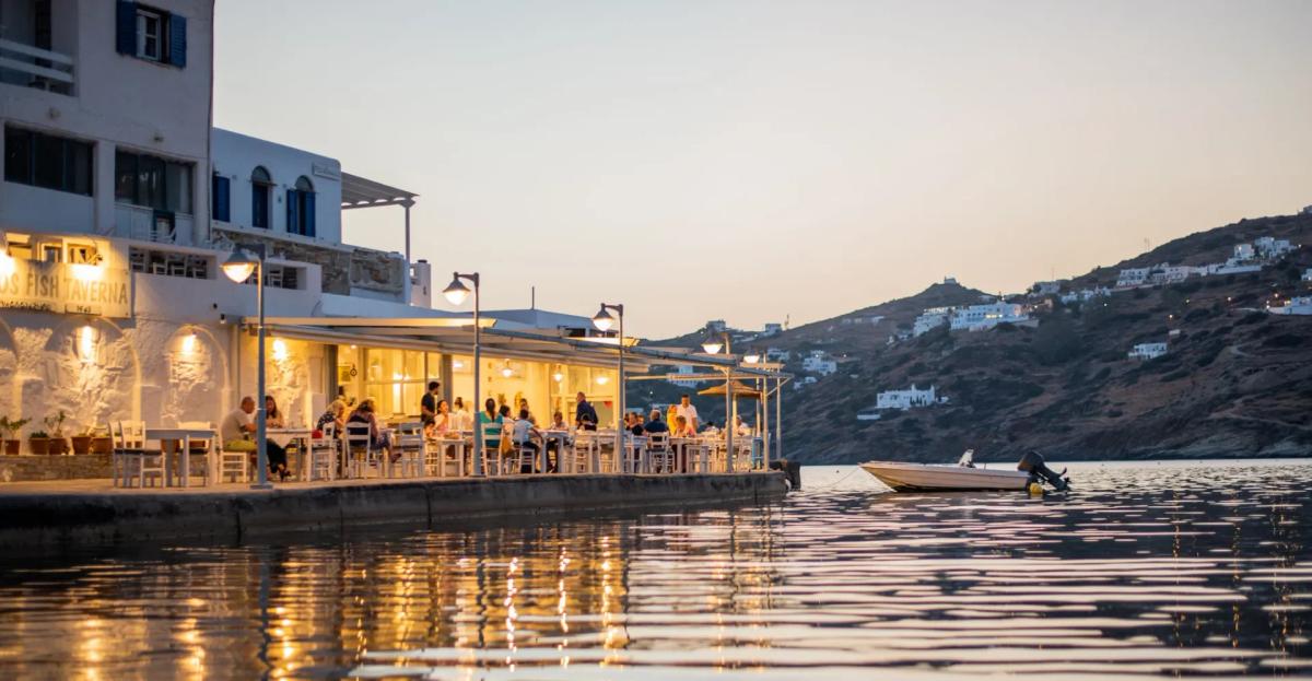 Drakos Taverna, Ios — waterfront tables at dusk at the far southern end of Mylopotas beach, lantern-lit tables on the pier and Aegean sunset over the bay