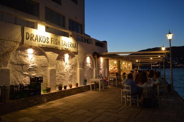 Drakos Fish Taverna sign lit up at night above the whitewashed frontage on Mylopotas beach, Ios
