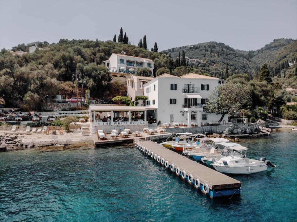 Aerial view of The White House at Kalami Bay, Corfu — the taverna and dock with boats moored on turquoise water below the wooded hillside