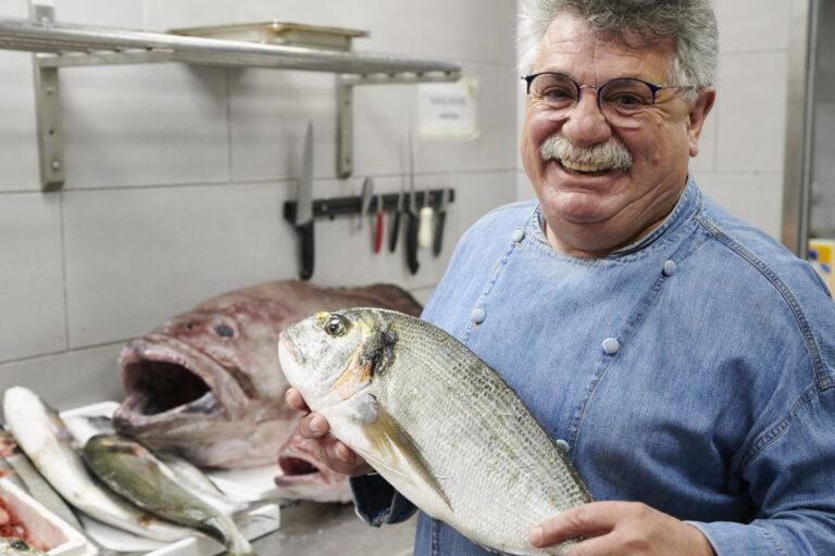 Chef at The White House holding a freshly caught sea bream in the kitchen, with the day's catch on ice behind him