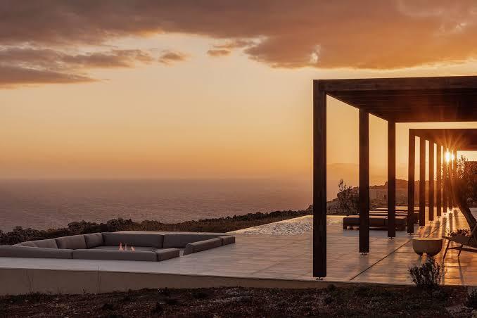 Gundari clifftop terrace at sunset — sunken firepit lounge and pergola on the edge of the cliff, looking out over the Aegean at golden hour