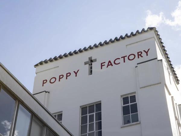 The Poppy Factory, Richmond — the white Art Deco frontage on Petersham Road with 'POPPY FACTORY' lettering in red beside a small cross, set against a bright sky