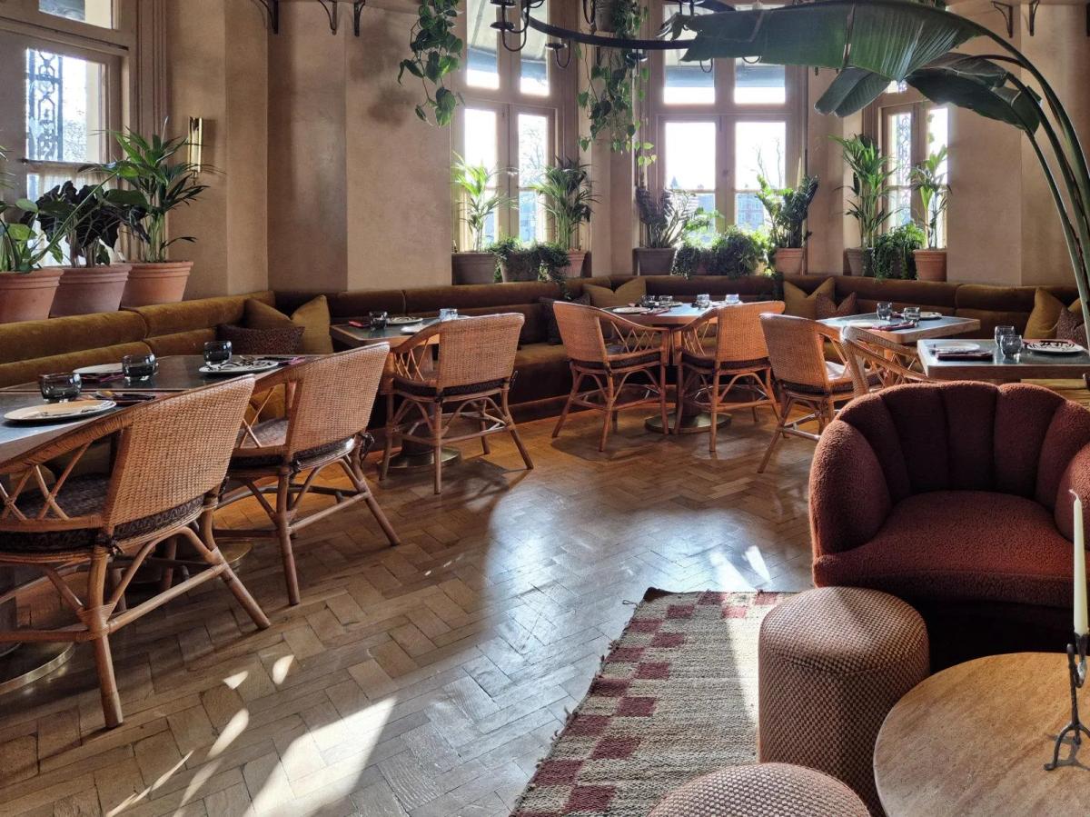 Tower House, Richmond — the glass garden room dining area with terracotta walls, wicker chairs, olive-velvet banquettes, potted palms and trailing plants in the tall arched windows